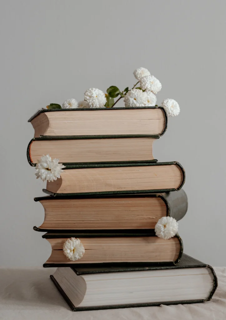 Stos starych książek ozdobiony białymi kwiatami.
